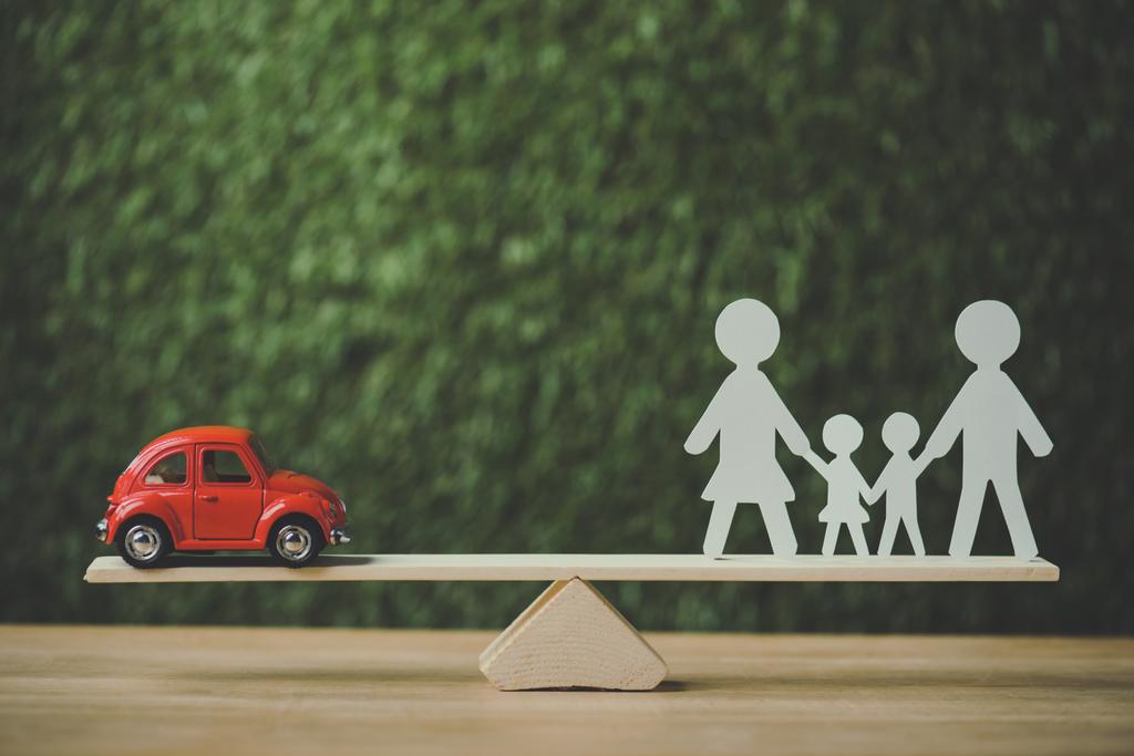 czerwony miniaturowy samochód i papier cięcia rodziny równoważenia na huśtawce na zielonym tle - Zdjęcie, obraz