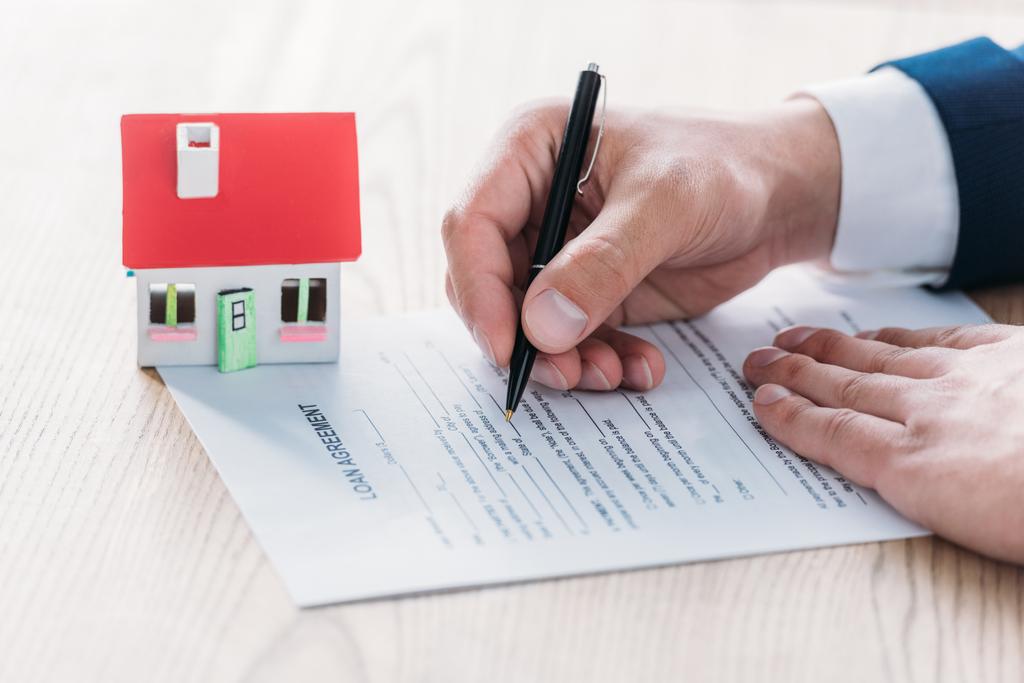 vue partielle de l'écriture d'agent immobilier dans l'accord de prêt près du modèle de maison sur le dessus de table en bois
 - Photo, image