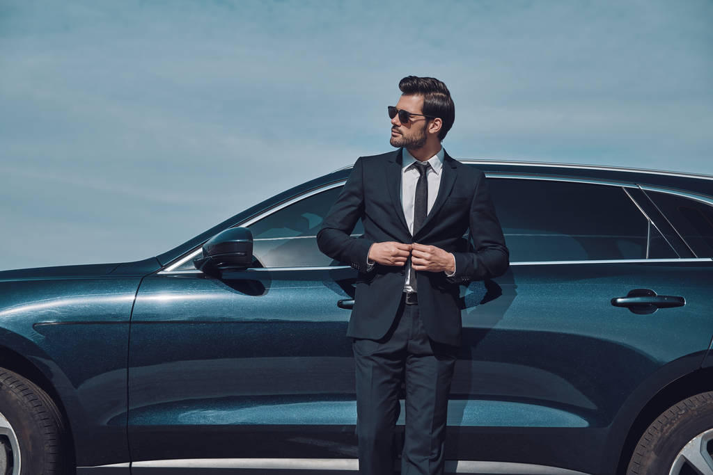 immer mit Stil. schöner junger Geschäftsmann passt Jacke an, während er im Freien neben seinem Auto steht - Foto, Bild
