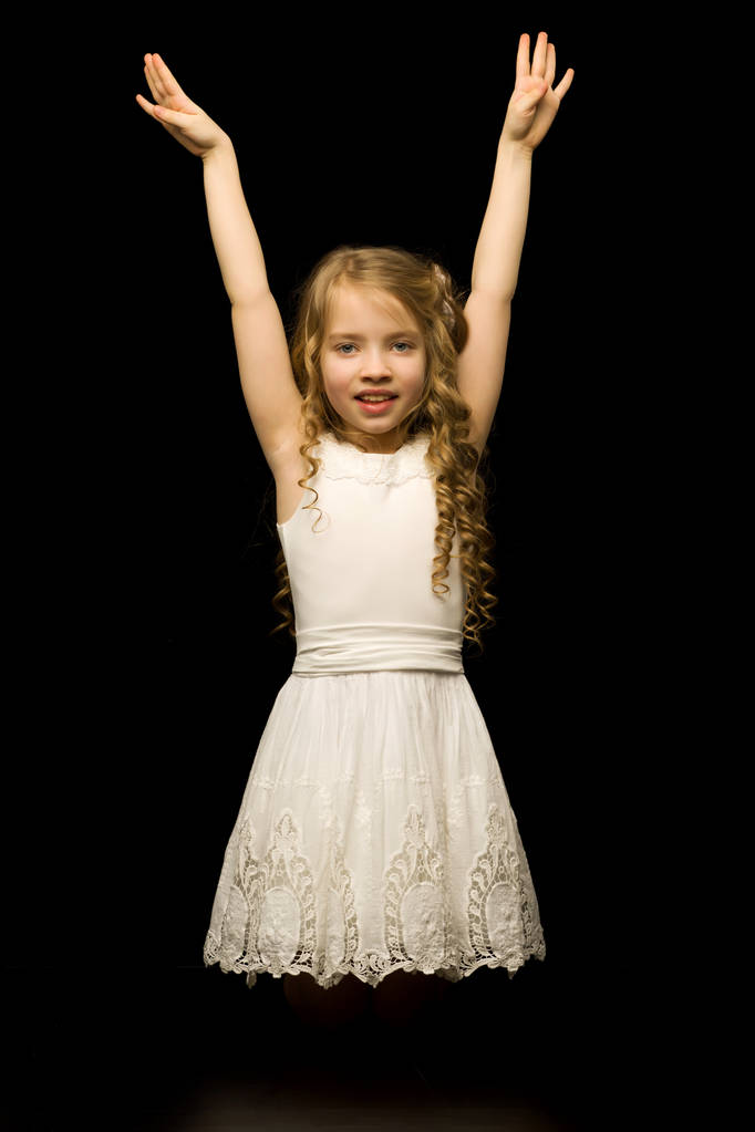 Маленькая девочка стоит на коленях на черном фоне в студии. - Фото, изображение