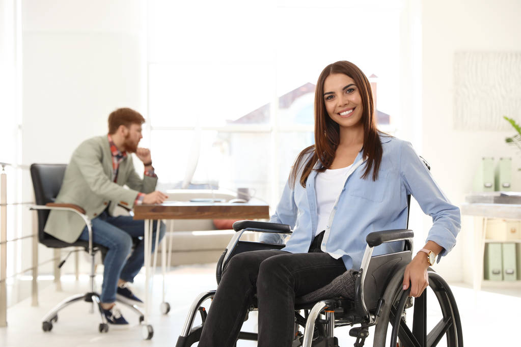 Nuori nainen pyörätuolissa kollegansa kanssa toimistossa
 - Valokuva, kuva