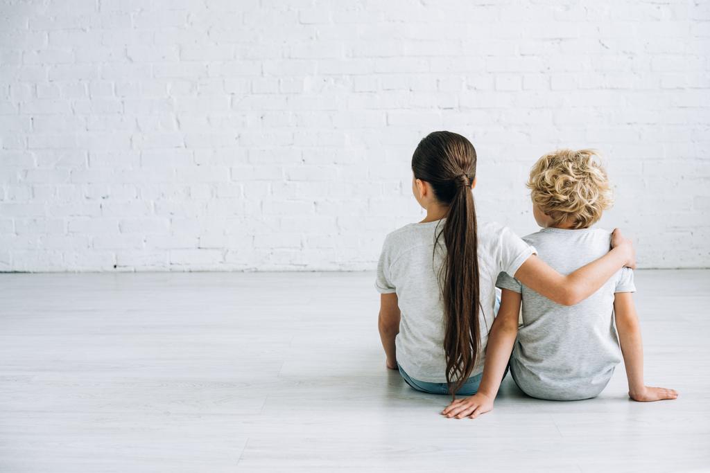 back view of two kids embracing on floor at home - Photo, Image