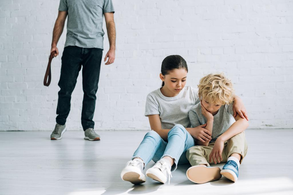 osittainen näkemys väkivaltainen isä ja surullinen lapset istuu lattialla
 - Valokuva, kuva