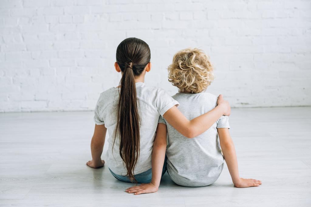 back view of two kids embracing on floor at home - Photo, Image