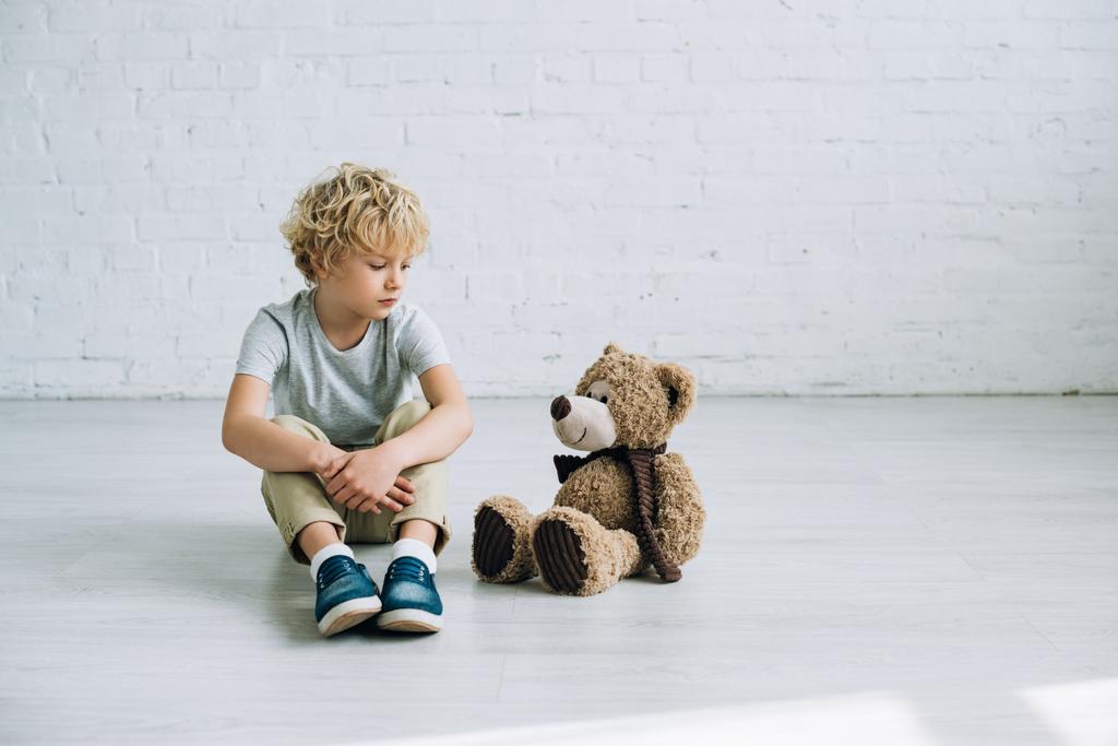 λυπηρό Προεφηβικό αγόρι με αρκουδάκι κάθεται στο πάτωμα - Φωτογραφία, εικόνα