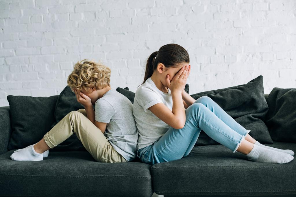 kaksi surullista lasta istuu sohvalla olohuoneessa
 - Valokuva, kuva