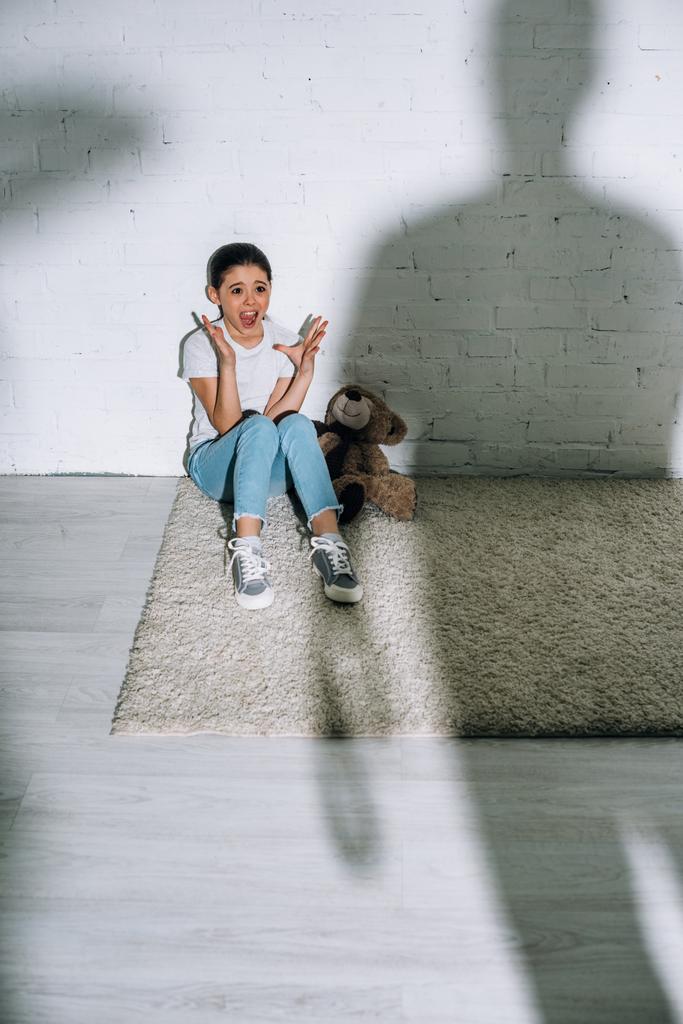 Velká silueta a vystrašená holka s medvídkem, jak křičí na koberec  - Fotografie, Obrázek