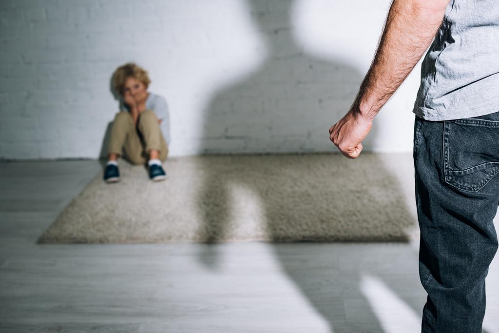 vista parcial del padre abusivo y el hijo asustado sentado en la alfombra
 - Foto, imagen
