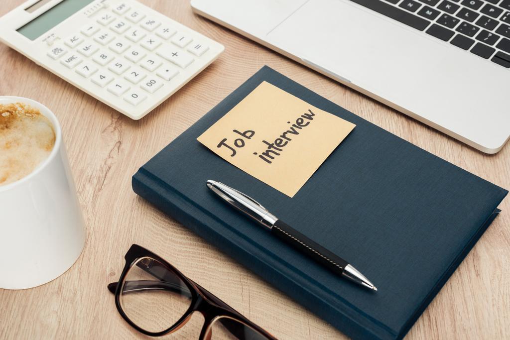 flache Liege mit Notizbuch mit Aufschrift auf klebrigem Zettel auf Holztisch mit Laptop, Schreibwaren, Gläsern und Kaffeetasse - Foto, Bild