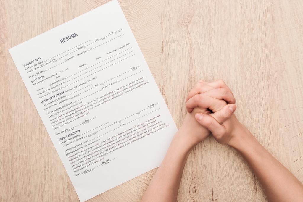 bijgesneden weergave van recruiter vasthouden gebalde handen in de buurt van CV sjabloon op houten tafel - Foto, afbeelding
