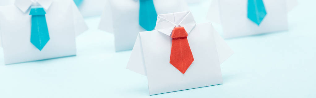panoramic shot of origami white shirts with blue ties with one red, leadership concept - Photo, Image