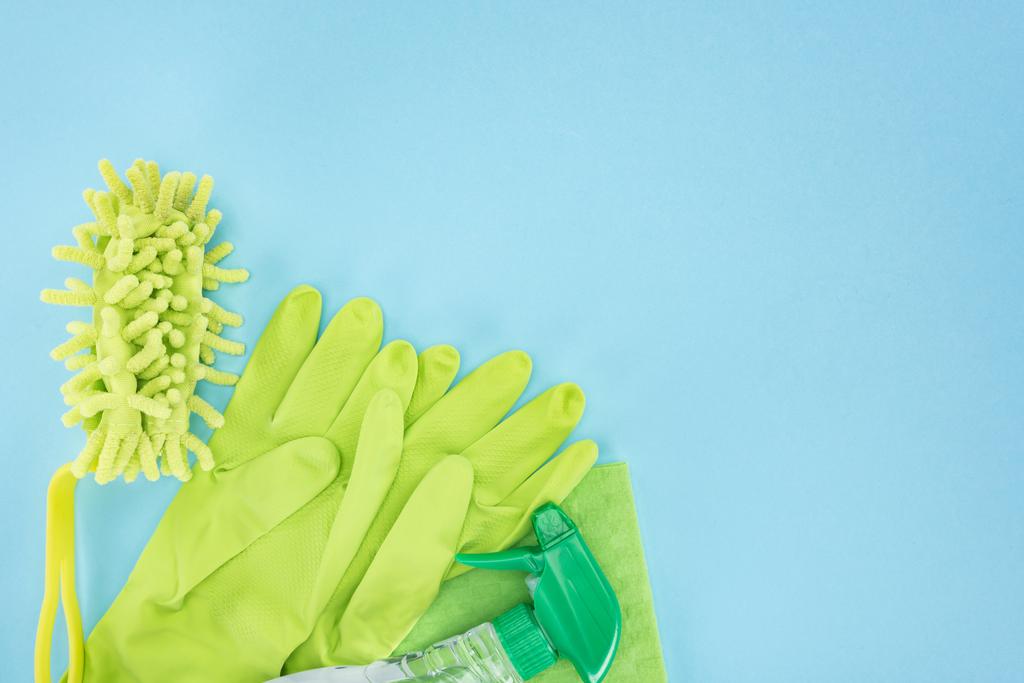 Κορυφαία όψη των πράσινων ελαστικών γάντια, σφουγγάρι, πανί και φιάλη ψεκασμού με απορρυπαντικό σε μπλε φόντο με χώρο αντιγραφής - Φωτογραφία, εικόνα