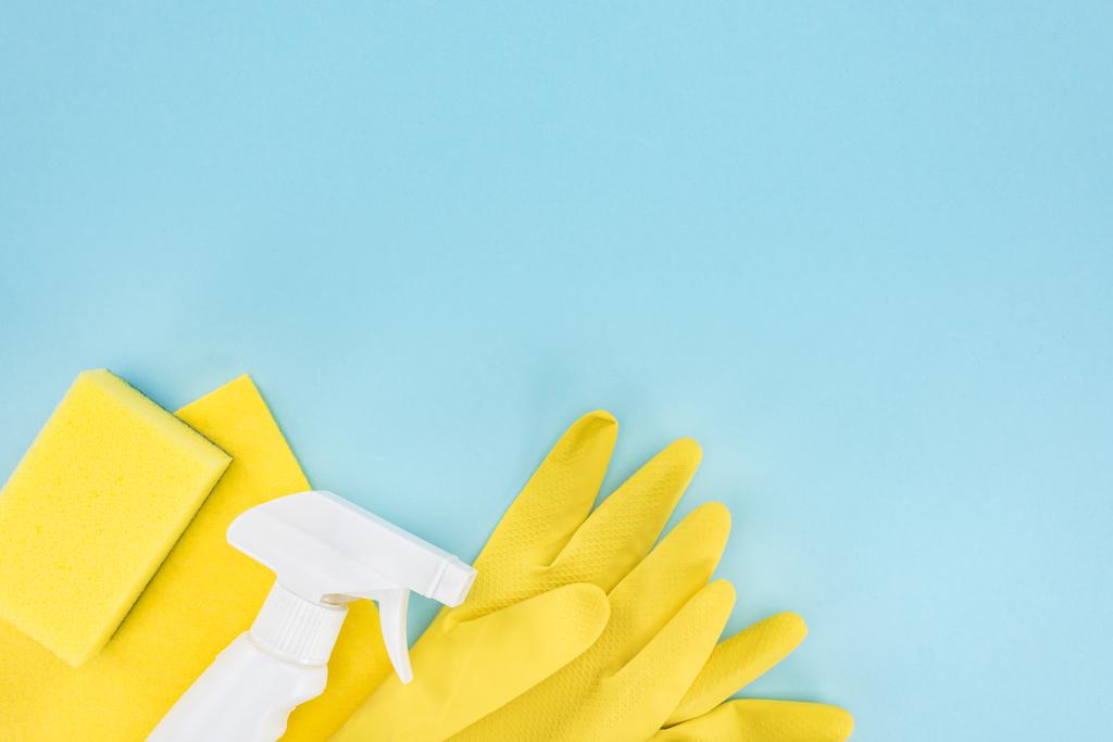 Ansicht von gelben Gummihandschuhen, Schwamm, Lappen und Spray auf blauem Hintergrund mit Kopierraum - Foto, Bild