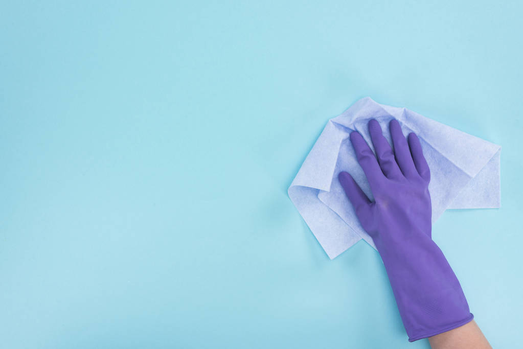 abgeschnittene Ansicht von Reiniger in lila Gummihandschuh hält Lappen auf blauem Hintergrund - Foto, Bild