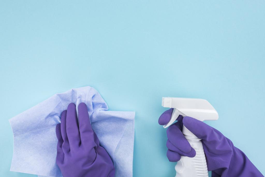 vista cortada de limpador em luvas de borracha roxa segurando pano e frasco de spray com detergente em fundo azul
 - Foto, Imagem