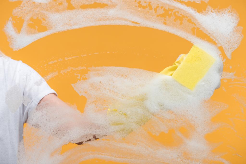 cropped view of cleaner in rubber glove cleaning glass with sponge on orange background - Photo, Image
