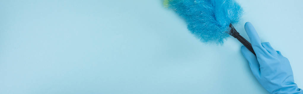 πανοραμική βολή καθαρότερο σε ελαστικό γάντι κρατώντας ξεσκόνισμα σε μπλε φόντο - Φωτογραφία, εικόνα