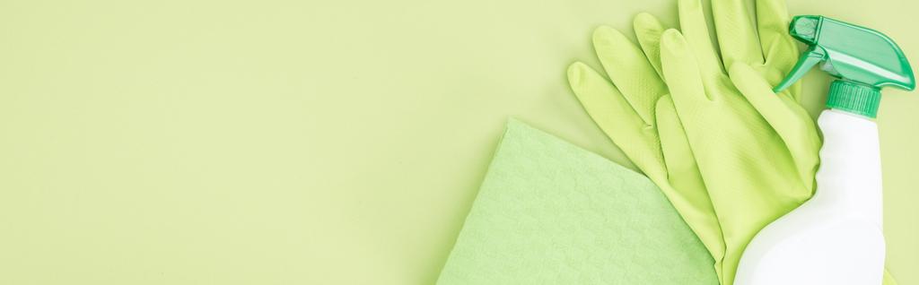 緑の背景に緑のゴム手袋、ぼろぼろとスプレーボトルのパノラマショット - 写真・画像