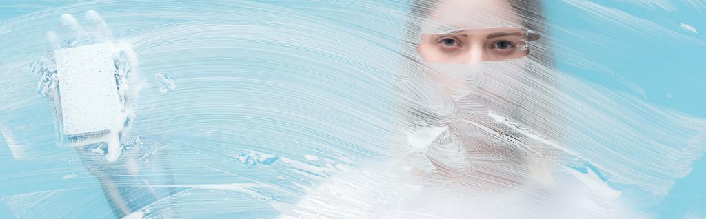 panoramic shot of woman eyes looking through glass with white foam on blue background - Photo, Image
