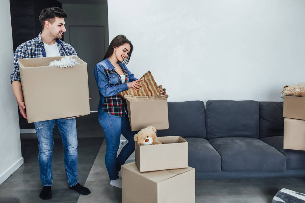 Homem feliz e mulher desempacotando coisas de caixas de desenhos animados enquanto mobiliário interior
 - Foto, Imagem
