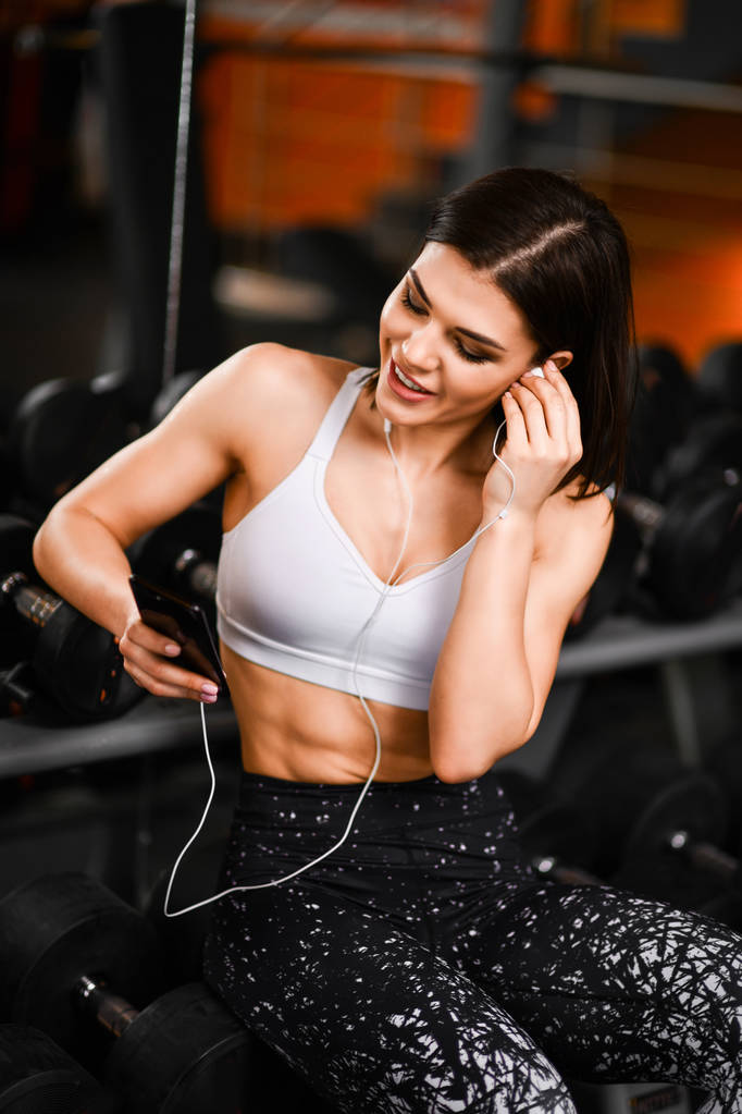 Porträt einer jungen Sportlerin mit Smartphone, die im Fitnessstudio Musik hört. - Foto, Bild