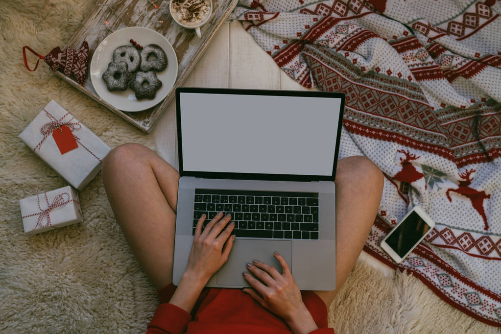 Disfrutando de la Navidad en casa. Mujer joven que trabaja en el ordenador portátil y beber café mientras está sentado en un piso en casa. Imagen de maqueta de vista superior de niña usando y escribiendo en el ordenador portátil con pantalla blanca en blanco
. - Foto, Imagen