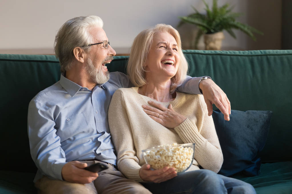 Laughing aged couple, man and woman watching tv and eating popcorn - Photo, Image