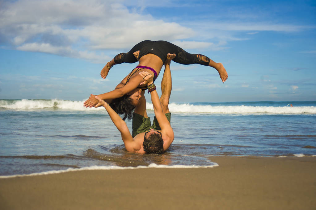 νεαρό ελκυστικό και συμπυκνωμένο ζευγάρι ακροβάτες εξάσκηση acro γιόγκα ισορροπία και διαλογισμό άσκηση στην όμορφη παραλία κάτω από ένα μπλε ουρανό στο μυαλό και τον έλεγχο του σώματος - Φωτογραφία, εικόνα