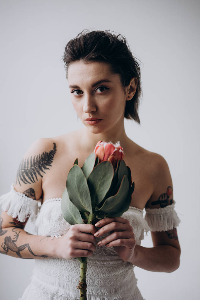  aantrekkelijke vrouw kijkend naar de camera op lichte achtergrond en het houden van exotische bloem in de handen - Foto, afbeelding