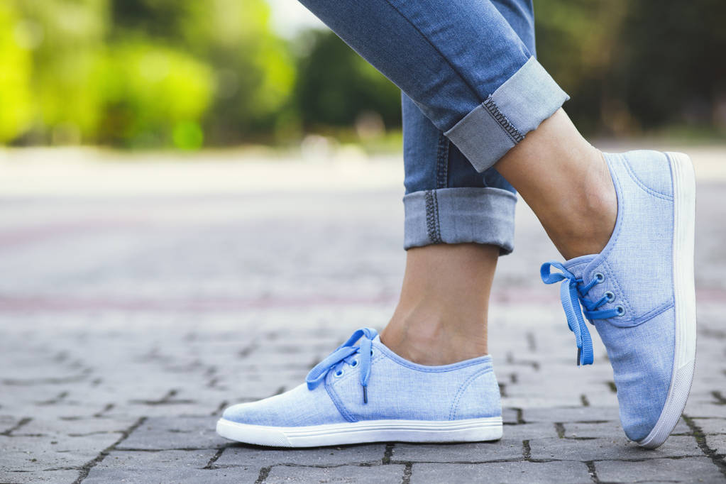 jambes d'une fille en jean et baskets bleues sur un carreau de trottoir, une jeune femme se promenant dans un parc d'été
 - Photo, image