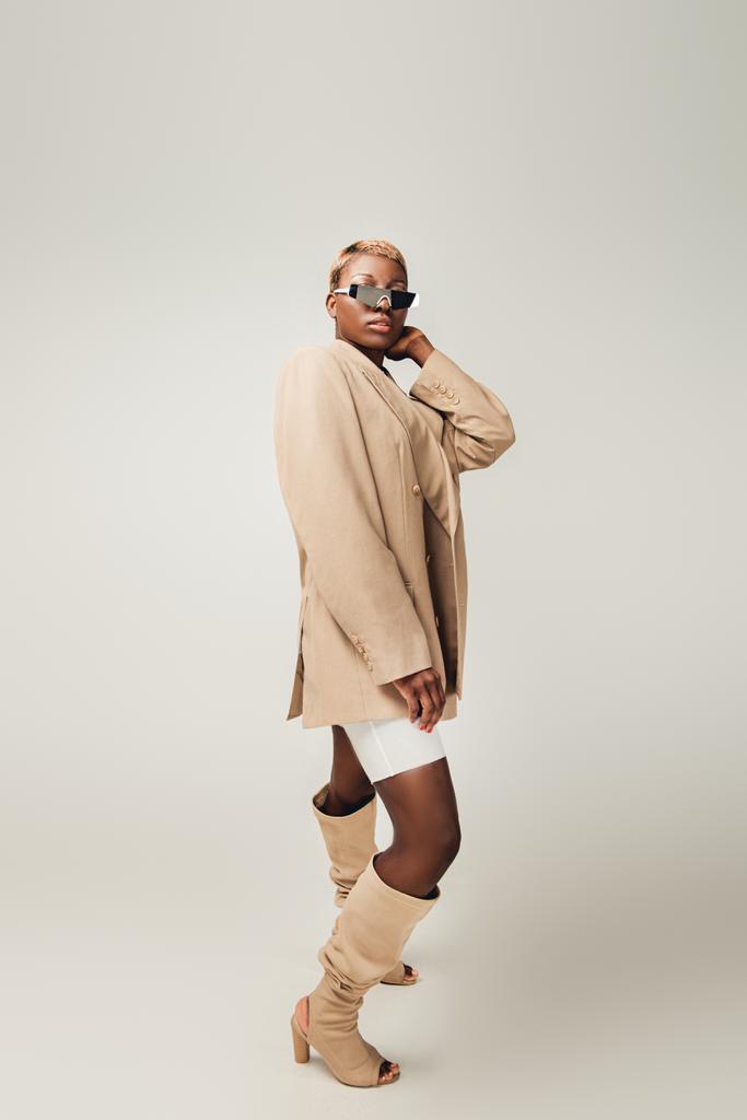 fille afro-américaine à la mode posant dans des lunettes de soleil et veste beige sur gris
 - Photo, image