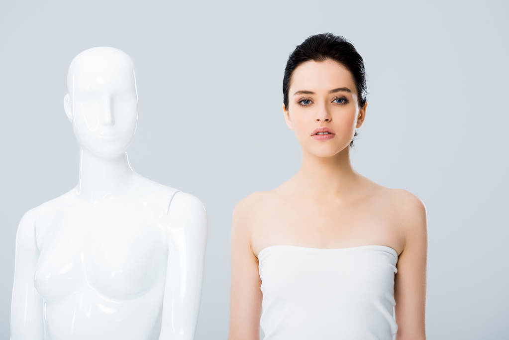 aantrekkelijke jonge vrouw in wit poseren met mannequin geïsoleerd op grijs - Foto, afbeelding