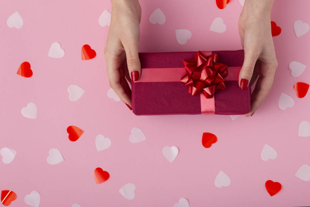 γυναικεία χέρια με ένα κουτί δώρου σε παστέλ χρωματισμένο φόντο επάνω όψη, το κορίτσι που κρατά ένα δώρο με διακοσμήσεις, η έννοια των αργιών και της αγάπης - Φωτογραφία, εικόνα
