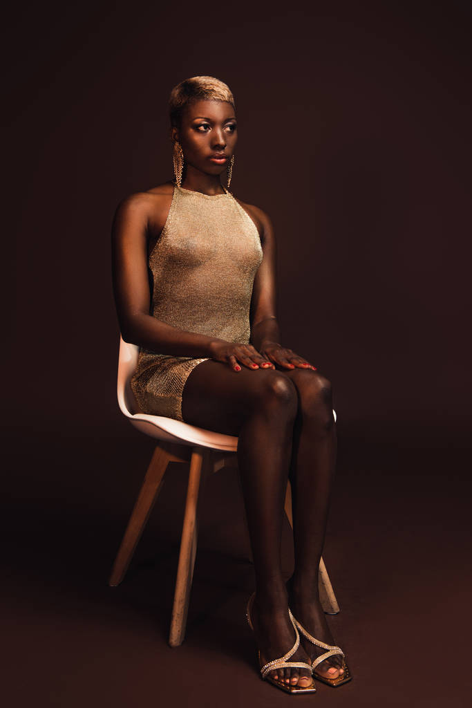 krásná elegantní africká americká žena s krátkými vlasy na židli na hnědém - Fotografie, Obrázek