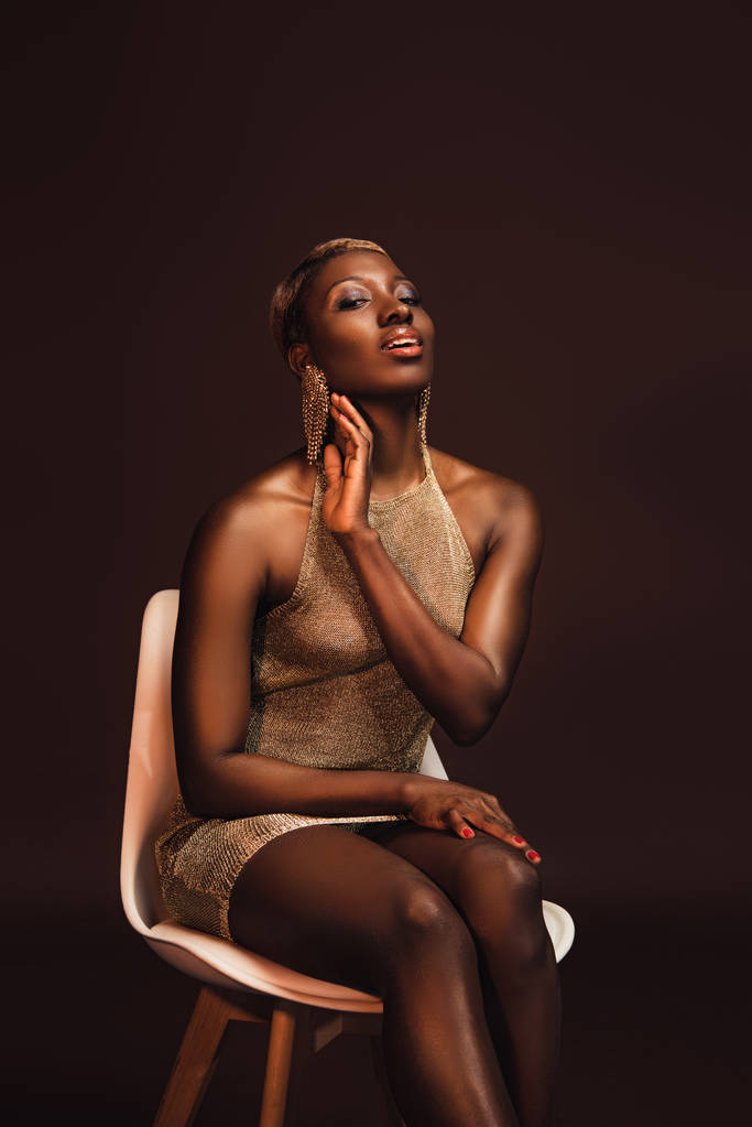 приваблива афроамериканська жінка сидить на стільці ізольована на коричневому
 - Фото, зображення