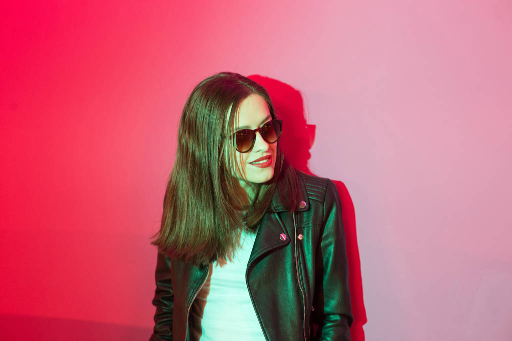 Vágású lány bőrkabát sötét szemüveget rózsaszín és kék neonfények háttér.  - Fotó, kép