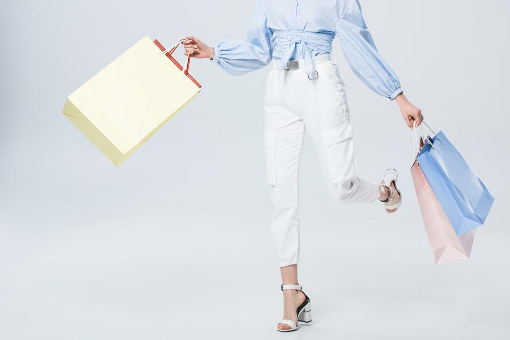 Обрезанный вид на стильную девушку, идущую с пакетами для покупок на сером
 - Фото, изображение