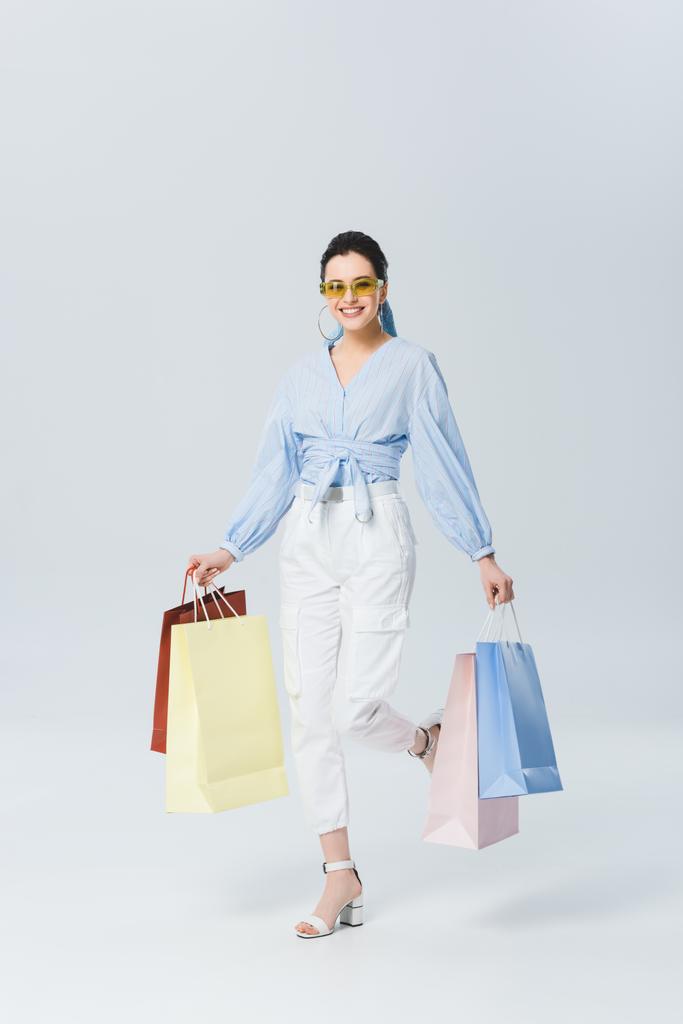 mooi glimlachend meisje met boodschappentassen wandelen op grijs - Foto, afbeelding