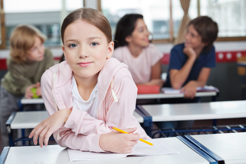 Schulmädchen stützt sich auf Schreibtisch mit Studenten im Hintergrund - Foto, Bild