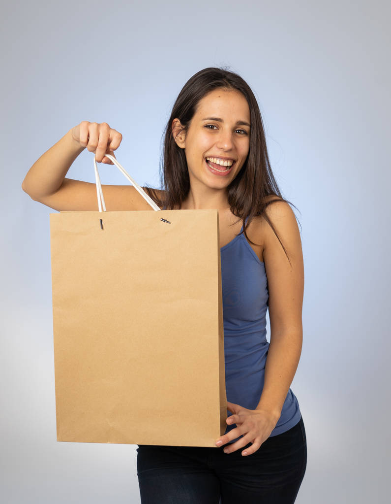 Mladá hezká Latinská žena, která zobrazuje a drží nákupní tašku s prázdným opčním prostorem připravenej na inzerát v prodeji speciální dary recyklovatelné papírové sáčky módní a kosmetické nakupování. Studiová střela. - Fotografie, Obrázek