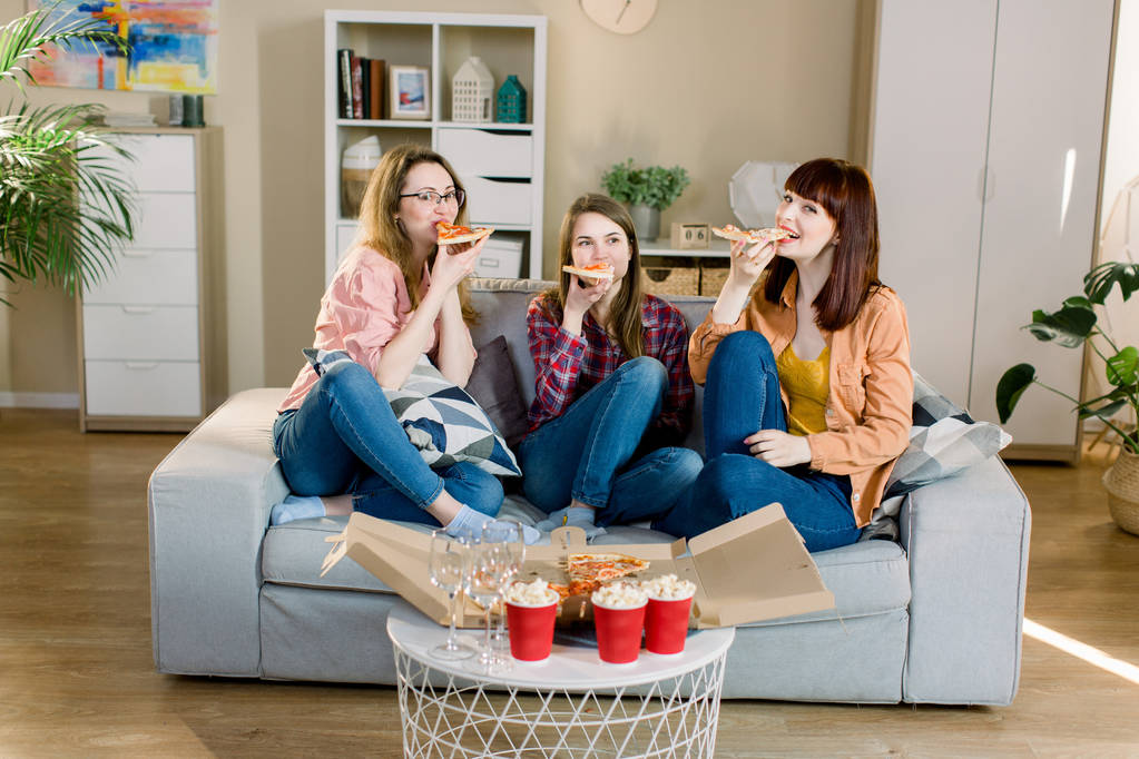 Group of three young female friends with pizza and popcorn celebrating in home interior - Photo, Image