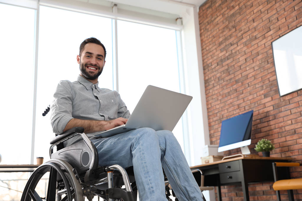 Ofiste dizüstü bilgisayar ile tekerlekli sandalyede genç adam portresi - Fotoğraf, Görsel