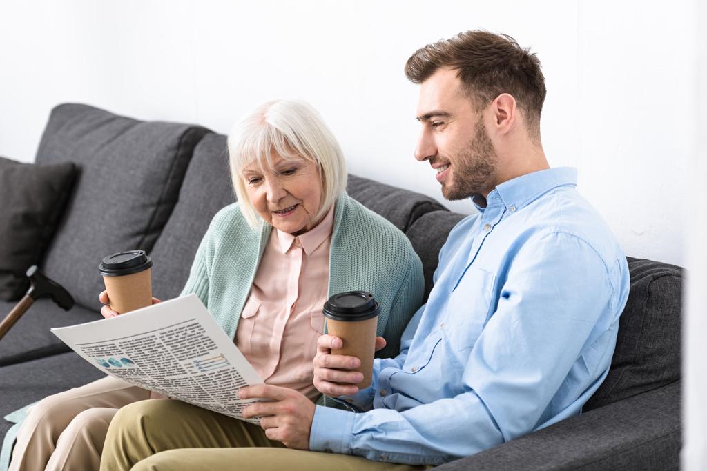 man and senior mother holding coffee and reading newspaper at home - Photo, Image