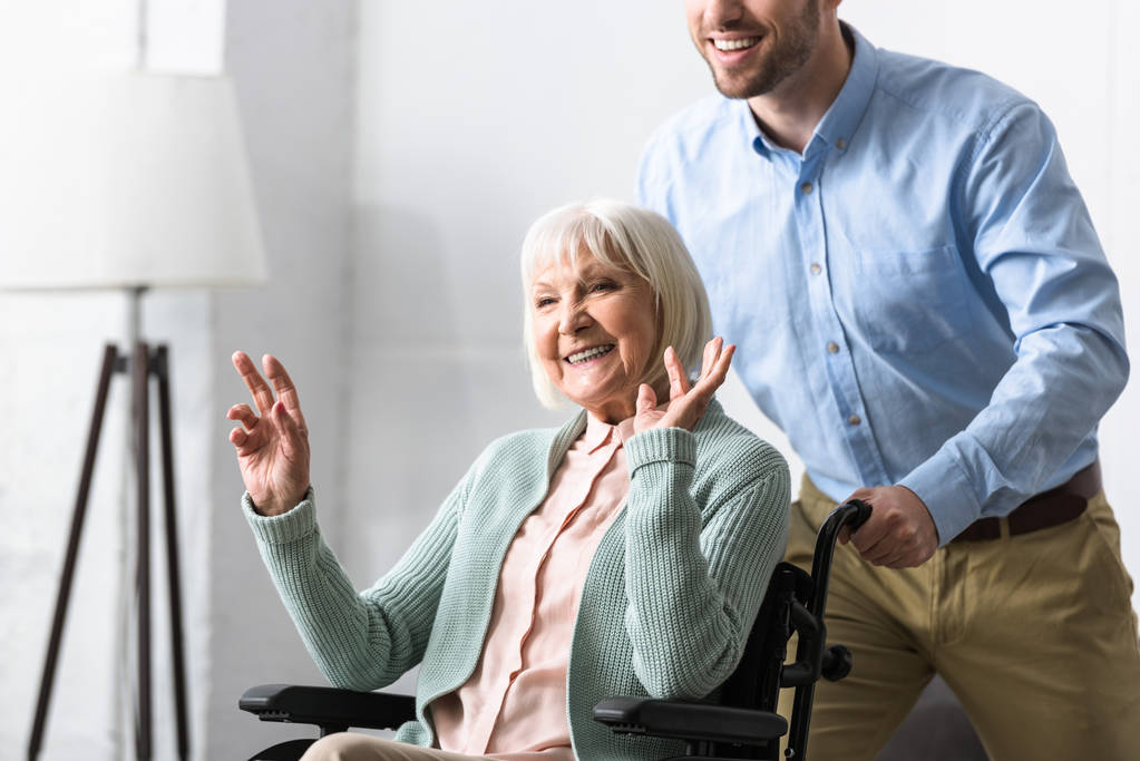Mann trägt behinderte Seniorin im Rollstuhl - Foto, Bild