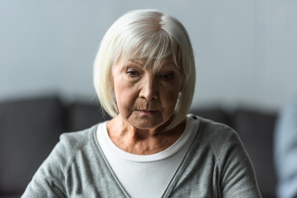 Nachdenkliche Seniorin mit grauen Haaren blickt nach unten - Foto, Bild