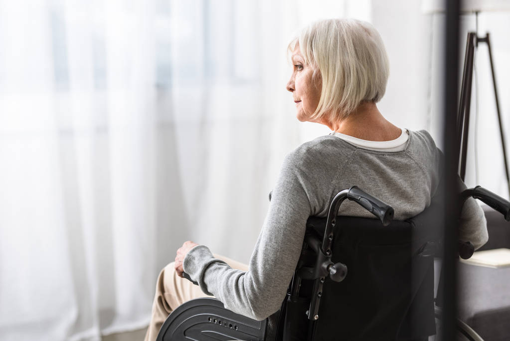 mujer mayor discapacitada pensativa sentada en silla de ruedas y mirando hacia otro lado
 - Foto, Imagen