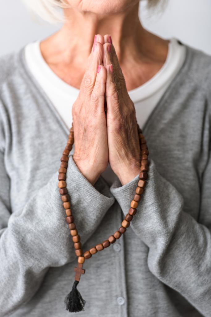 частичный взгляд пожилой женщины, молящейся с деревянными четками
 - Фото, изображение