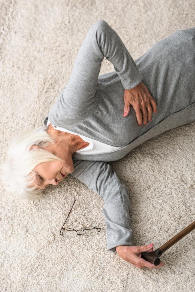 overhead view of sick senior woman with walking stick lying on carpet - Photo, Image