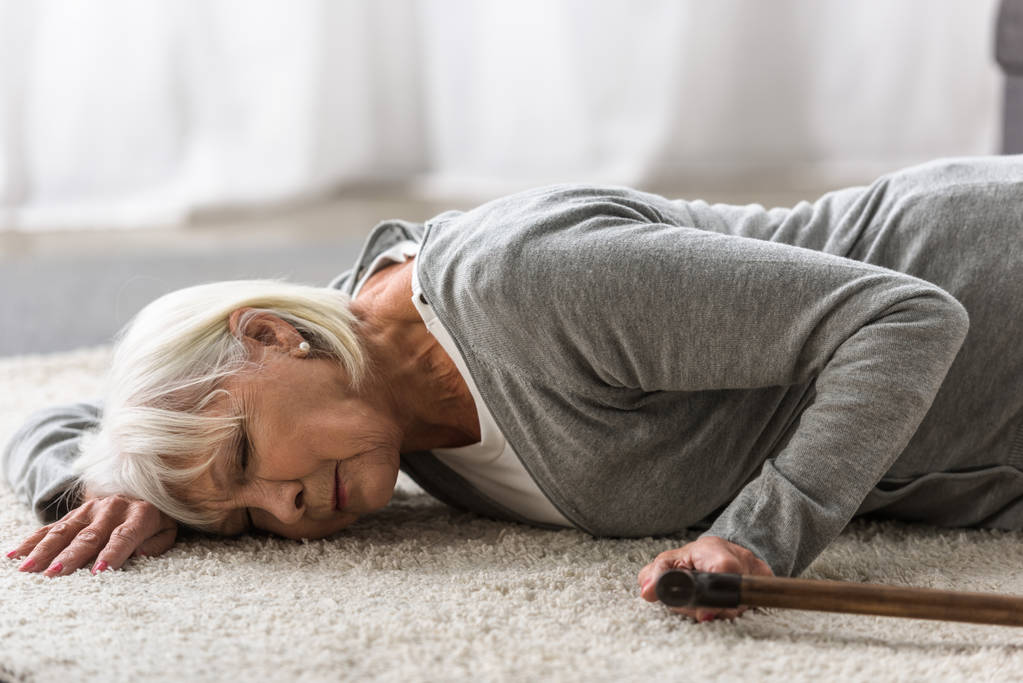 хвора старша жінка з тростиною лежить на килимі з закритими очима
 - Фото, зображення