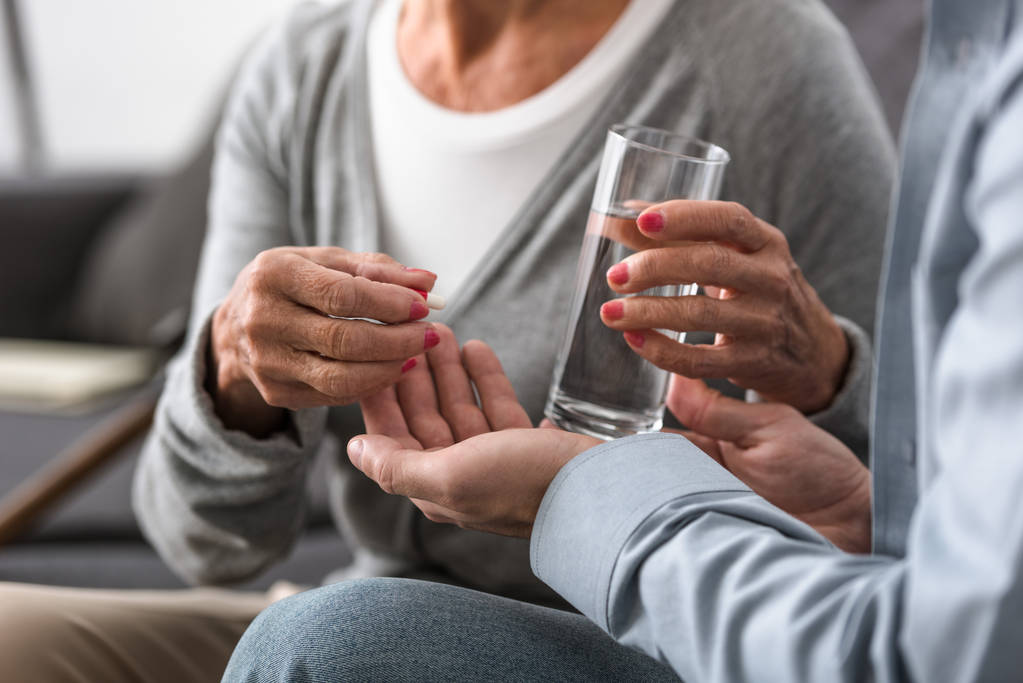 обрезанный вид человека, дающего старшей матери стакан воды и лекарства
 - Фото, изображение